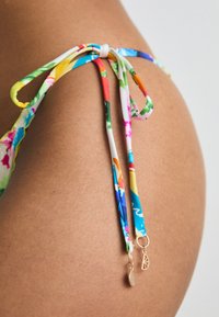 Krāsainas bikini sasiešanas ar ziedu rakstiem, kas izgatavotas no auduma, aprīkotas ar cilpām un zelta aksesuāriem drošai aizdarei. Gluda ādas fona.