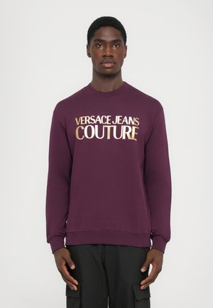 Lila Sweatshirt mit goldenem "VERSACE JEANS COUTURE" Schriftzug, Rundhalsausschnitt, gerippte Bündchen und Saum sowie einer weichen, strukturierten Oberfläche.