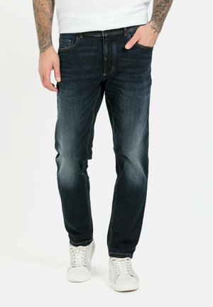 Dark blue denim jeans with a classic fit, light fading on thighs, contrast stitching, five pockets, worn with white sneakers.