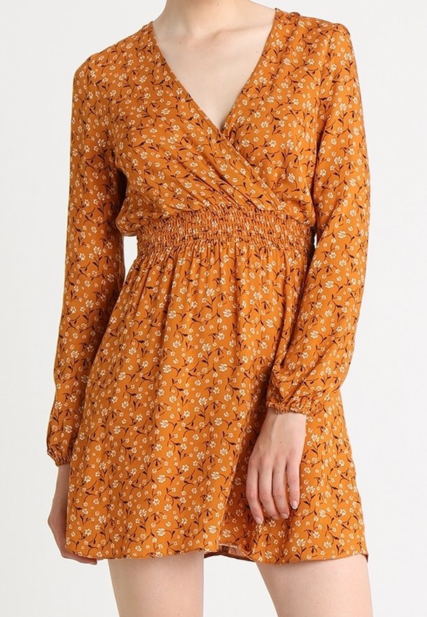 Ruskofärgad blommig klänning med långa ärmar, v-ringning och smockad midja. Har spridda vita och gula blommor på lätt tyg.
