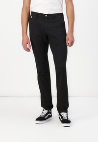Black straight-leg pants made of cotton fabric, featuring a zip fly, button closure, and front pockets, paired with black and white sneakers.