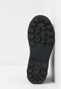 Semelle de chaussure en caoutchouc noir avec un design texturé et motif. Présente des reliefs profonds pour l'adhérence. Nom de la marque "Camper" embossé sur le côté.