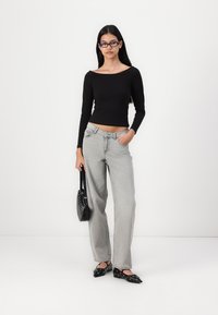 Black long-sleeve top, light grey wide-leg jeans, black pointed flats with studs, and a small black handbag. Smooth fabric and tailored fit.