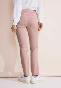 Ljusrosa byxor i stretchbomull med två bakfickor och tapered ben-design, tillsammans med vita sneakers.