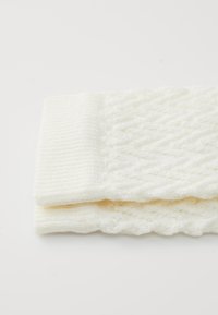 Close-up van gevouwen witte gebreide wollen sokken met gestructureerde ruiten en ribbelpatronen op een witte achtergrond.