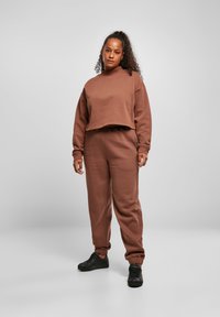 Hnedý skrátený svetrový top s vysokým golierom a voľným strihom, doplnený o zodpovedajúce zúžené tepláky. Čierne tenisky dotvárajú look.
