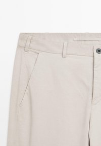 Light beige pants with a flat front, angled pockets, a button closure, and belt loops. Made from a smooth, woven fabric.