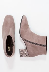 Szare zamszowe botki za kostkę mają boczny zamek błyskawiczny oraz ozdobny blokowy obcas z metalicznymi akcentami i dekoracyjnym wzorem.