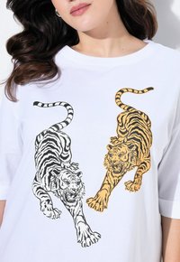T-shirt blanc avec un design graphique de deux tigres : l'un noir et blanc, l'autre orange avec des rayures noires, tous deux dans des poses dynamiques.