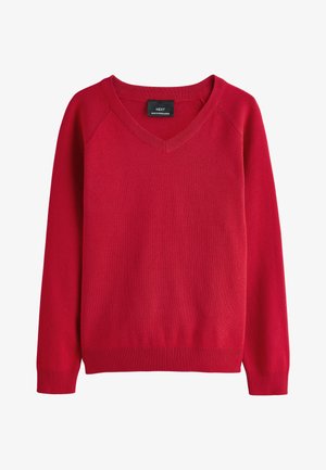 Dijete obučen u bijelu košulju s ovratnikom ispod crvenog džempera s V-izrezom, prikazano od brade do ramena na neutralnoj pozadini.