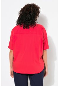 Blusa rossa a maniche corte con vestibilità ampia, colletto piatto e dettagli sulla parte posteriore. Tessuto liscio con una texture morbida.