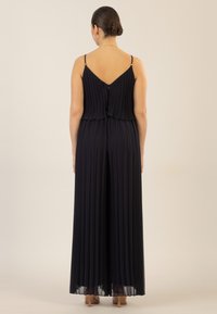 Mono de navy plisado con tirantes ajustables, diseño de espalda en V y detalle de falda abierta. Cuenta con un cierre de cremallera en la parte posterior.