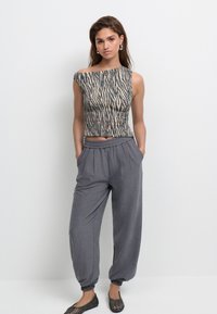 Bauchfreies Oberteil mit Zebramuster in Beige und Dunkelblau; kombiniert mit grauen, locker sitzenden Hosen mit elastischen Bündchen und Seitentaschen.