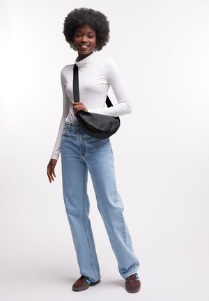 Bolso negro de bandolera con textura lisa; modelo con cuello alto blanco ajustado, vaqueros azul claro de talle alto y zapatillas marrones.