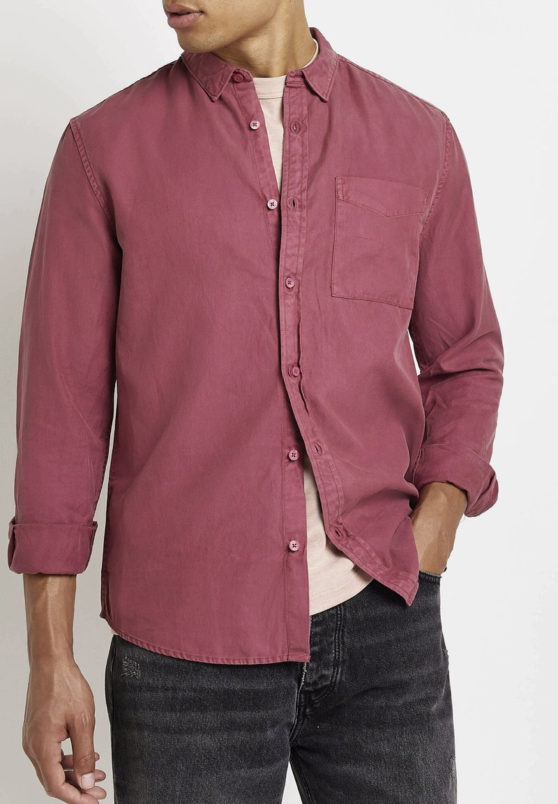 Camicia a maniche lunghe e bottoni di un borgogna tenue, realizzata in tessuto leggero. Presenta una tasca sul petto e maniche arrotolate.