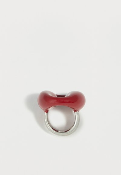 Bague en argent avec un détail en résine rouge lisse et épais en forme de deux lobes arrondis sur le dessus, sur fond blanc uni.