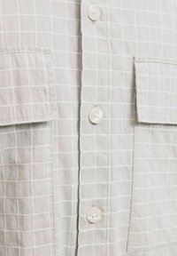 Camicia grigia chiaro con un motivo a griglia, dotata di due tasche sul petto e bottoni bianchi, realizzata in un tessuto testurizzato.