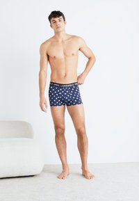 Tengerész kék boxer alsónadrág fehér és világoskék mintákkal, rugalmas derékrésszel, testhezálló stílusban, és puha pamut anyagból.