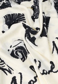 Tissu léger et transparent présentant des motifs abstraits noirs sur un fond crème. Texture douce avec un drapé fluide et des détails d'impression visibles.