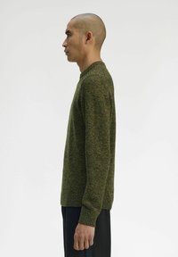Maglione verde lavorato a maglia con scollo rotondo, motivo testurizzato e polsini a coste, indossato con pantaloni neri. Presenta una silhouette aderente.