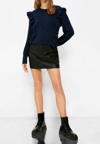 Maglione a maglia blu navy con dettagli arricciati, abbinato a una mini gonna in pelle nera e stivaletti neri con lacci e suola spessa.