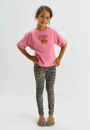 Vaaleanpunainen puuvillainen t-paita, jossa "Just Peachy" -grafiikka, yhdistetty leopardikuvioisiin leggingsseihin ja harmaisiin varvassandaaleihin. Malli poseeraa käsien ollessa lanteilla.