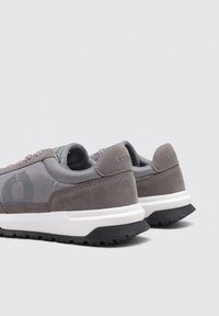 Zapatillas deportivas grises con una combinación de materiales lisos y gamuza, presentan una media suela blanca, una suela exterior negra texturizada y sutiles acentos de marca.