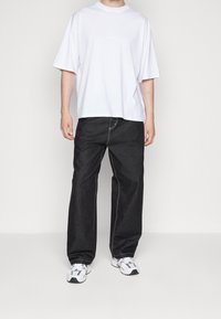 Camiseta de algodón blanca de manga corta, combinada con unos vaqueros de denim negros de corte holgado que tienen detalles de costura clara y un dobladillo sin terminar.