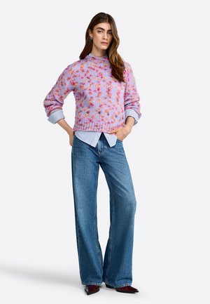 Maglione lavorato a maglia di un delicato color lilla con macchie rosa e arancioni, abbinato a una camicia a righe blu chiaro e jeans a gamba larga blu.