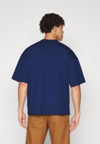 Námořnickomodré, oversize bavlněné tričko s krátkými rukávy a kulatým výstřihem. Hladký povrch; má jednoduchý, nezdobený design.