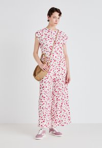 Tuta floreale bianca con fiori rossi e rosa; vestibilità ampia, maniche corte. Abbinata a una borsa intrecciata e sneakers rosa.