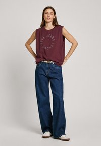 Burgundské bezrukávové tričko s kulatým potiskem "Pepe Jeans London", spárované s volnými tmavě modrými džíny a bílými teniskami.