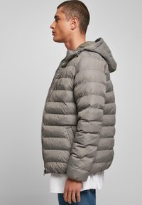 Grå dunjakke med quiltet design, hætte og lynlås. Materialet har en glat, blank finish med elastiske manchetter.
