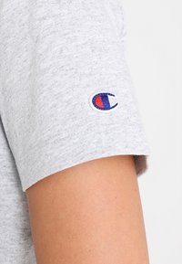 Grijze korte mouwen T-shirt gemaakt van katoen, met een geborduurd logo in blauw en rood op de mouw. Zachte textuur met een relaxte pasvorm.
