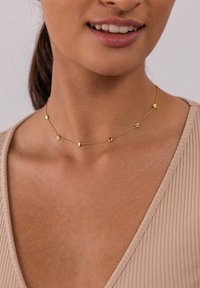 Goldkette mit kleinen dreieckigen Akzenten, ausgestattet mit einer zarten Kette und einem minimalistischen Design, liegt auf der Haut mit einem strukturierten Ausschnitt.