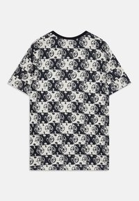Camiseta de manga corta en crema con un patrón de cuadrícula negra que presenta diseños circulares y signos de interrogación, escote redondo y textura suave.