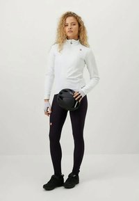 White zip-up cycling jacket, black leggings, gloves, and black helmet. The outfit features a slim fit with a textured jacket and flat seams.