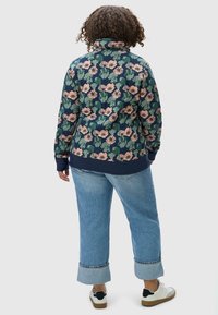 Giacca a pullover blu navy con motivo floreale, colletto alto, polsini e orlo a coste. Abbinata a jeans azzurri arrotolati e sneakers bianche.