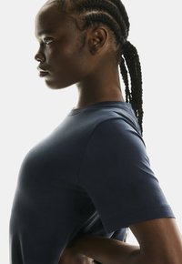 Sötétkék, rövid ujjú atletikai póló, sima, testhezálló fazonnal. Kerek nyakkivágással és finom textúrájú részletekkel rendelkezik az anyagon.