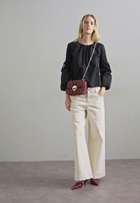 Haut noir à manches longues avec des manches bouffantes, associé à un pantalon large blanc et un sac bandoulière à motif bordeaux. Chaussures rouges à bout pointu.