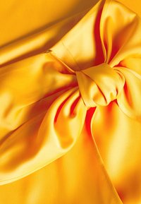 Tessuto giallo con una consistenza liscia, caratterizzato da un evidente dettaglio a fiocco al centro, accentuato da cuciture eleganti e colori vivaci.