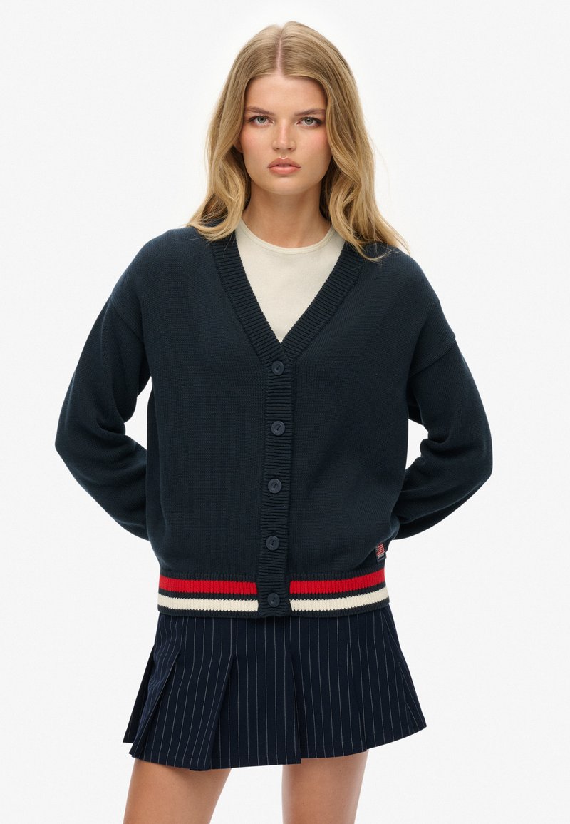 Cardigan en maille bleu marine avec un col en V, une fermeture à boutons et un ourlet à rayures côtelé. Possède des manches longues et une coupe décontractée.