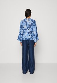 Blusa a fiori in toni di blu con maniche lunghe, abbinata a pantaloni larghi di un blu scuro. Tessuto testurizzato, silhouette rilassata.