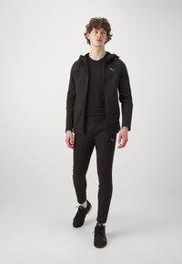Tuta atletica nera composto da una felpa con zip e pantaloni aderenti, caratterizzato da una texture liscia e finiture con logo discreti.