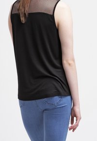 Top sin mangas negro con un respaldo de malla texturizada. Tela suave con un corte relajado, combinado con unos vaqueros azul claro ajustados, mostrando el detalle de la parte trasera.