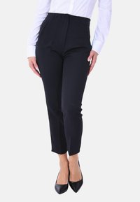 Pantaloni neri su misura con vita alta, caratterizzati da pieghe frontali e tasche laterali. Abbinati a una camicia bianca e tacchi a punta neri.