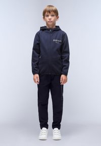 Marineblå zip-hoodie med logo-detalje, parret med matchende joggers og hvide sneakers. Har lange ærmer og en frontlynlås.