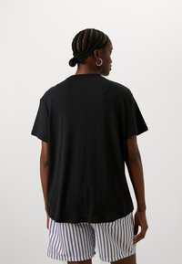 Czarna koszulka z krótkim rękawem i zaokrąglonym dekoltem, o miękkiej fakturze i z centralnym szwem, w połączeniu z pasiastymi szortami.