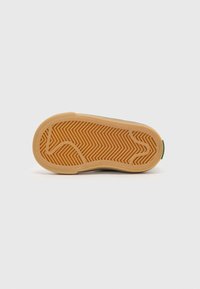 Herringbone mintázatú cipőtalp, bézs gumibázissal és zöld kiemeléssel a saroknál, lapos forma sima textúrával.