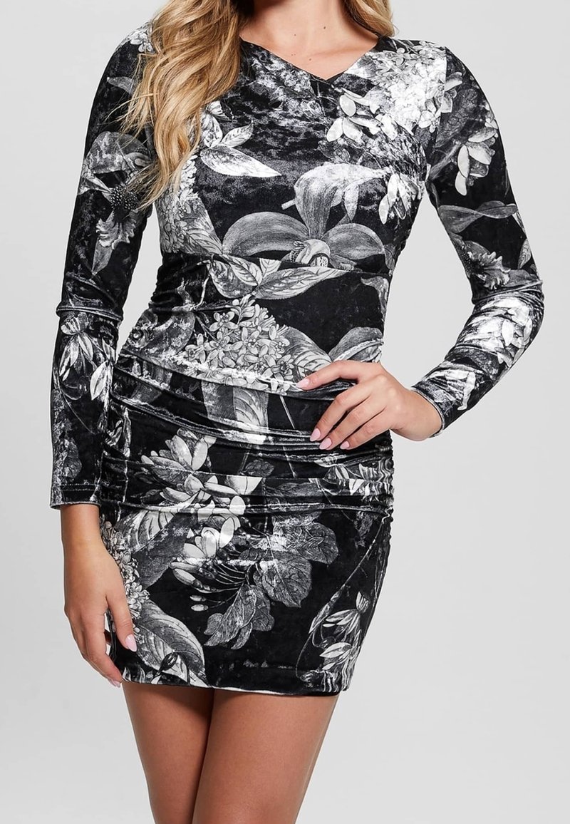 Zwarte mini-jurk met bloemenprint, een V-hals en lange mouwen. Gemaakt van een textuurstof met geplooide zijkanten en witte bloemenpatronen.